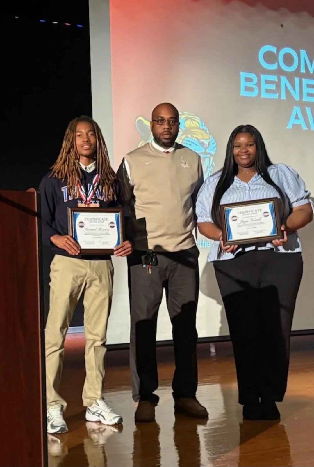 100 Tigers 2026 scholarship recipients holding their award certificates on stage with a Sussex Central staff member